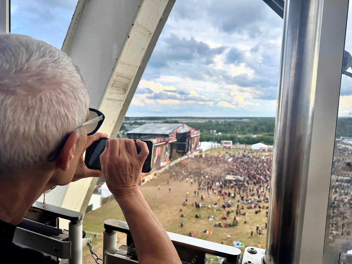 A trip participant takes a photo with her phone of the festival's main stage from inside the gondola of the Ferris wheel. The crowd and a large Pol'and'Rock sign can be seen in the background.